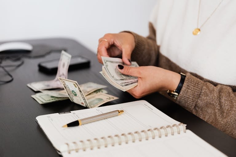 Managing Finances of Close-up of person counting cash with notepad on desk, indicating financial tasks.