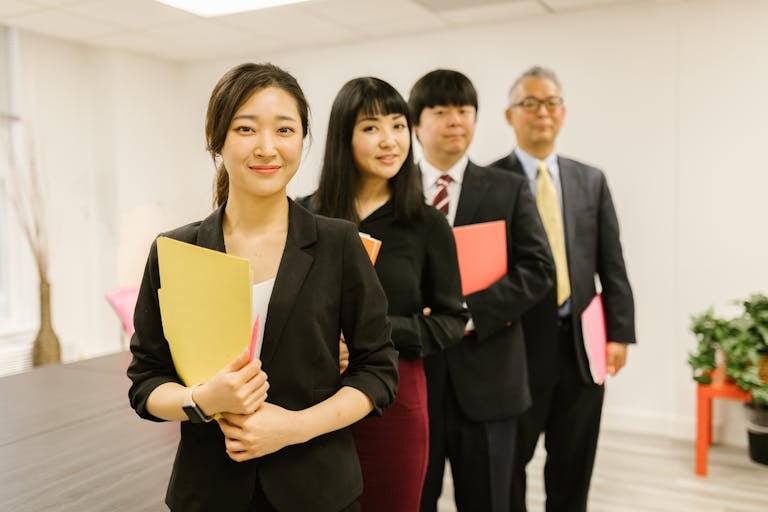 team alignment, A group of business professionals standing in an office holding documents, smiling confidently.
